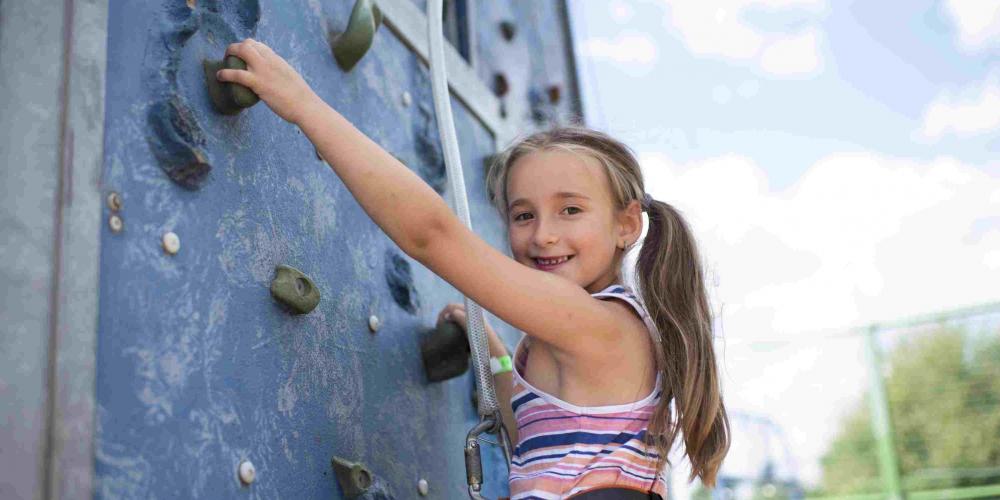A young girl is on a climbing wall while smiling