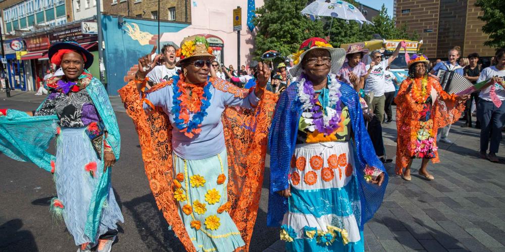 A group of ladies wearing colourful, cultural dress walk down the street as part of a parade