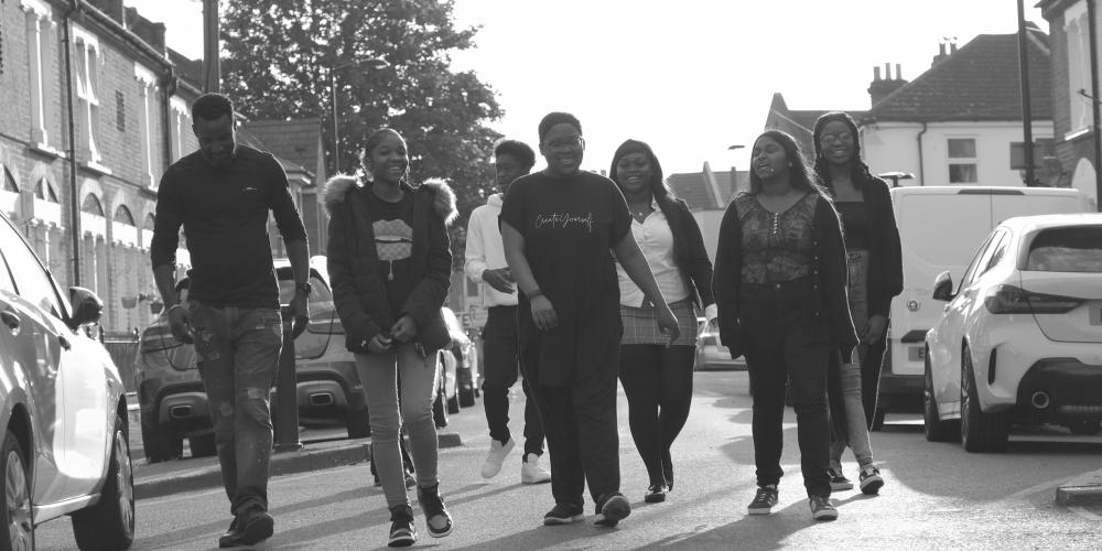 A blakc and white photo of a group of young people walking down the street. They are smiling and laughing